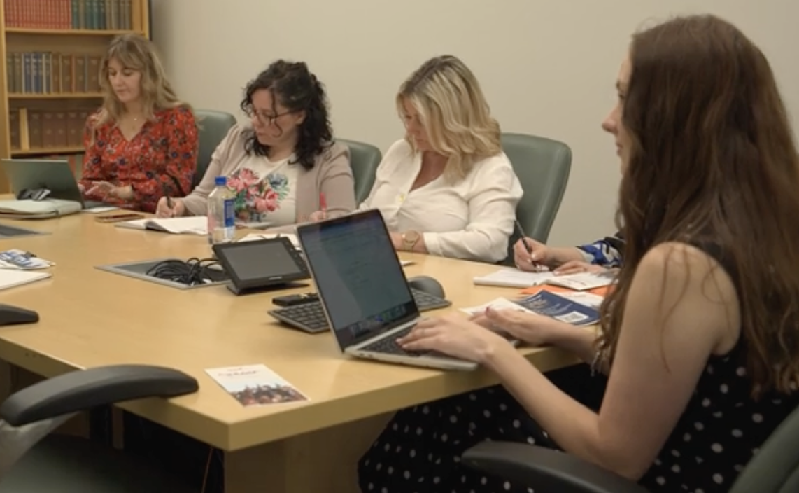 A group of women with computers and notepads sitting at a desk